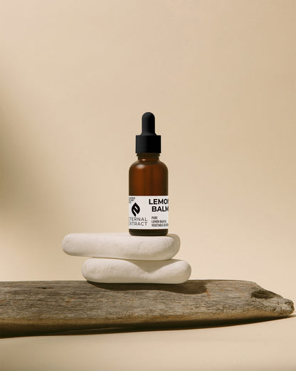A display of Lemon Balm Tincture by Sacred Plant Co, elegantly positioned on white stones and wooden texture, evoking the natural purity of the product