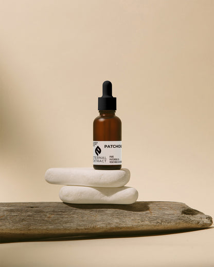 Artistic display of Sacred Plant Co Eternal Patchouli Extract, a natural skincare essential, on zen-like stones against a neutral background.