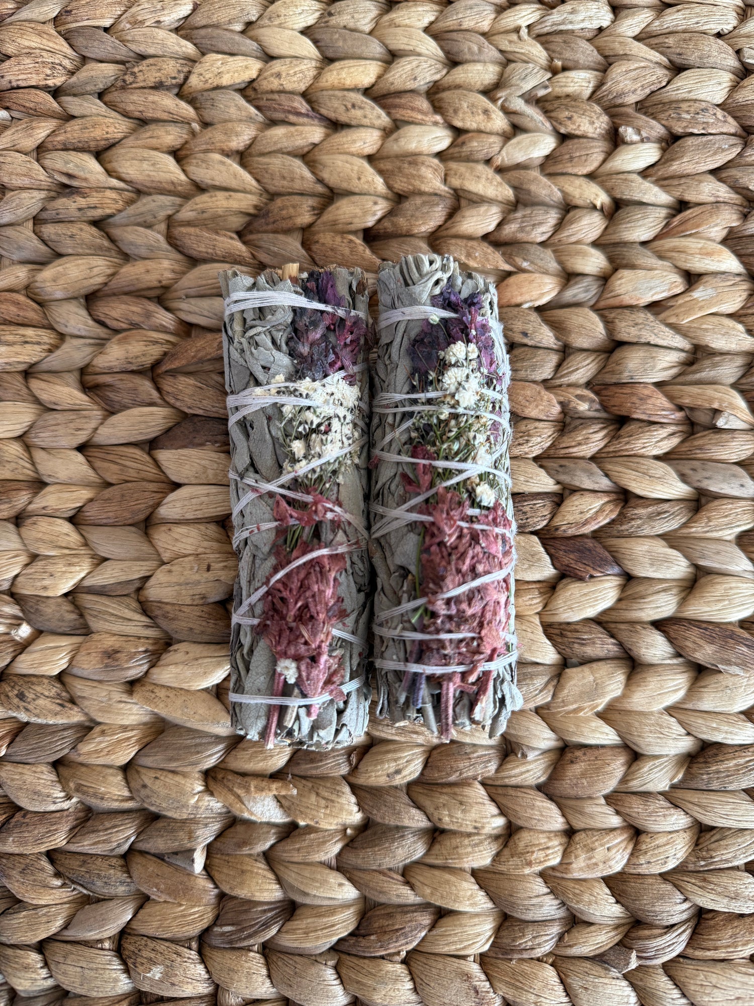 Pair of handcrafted consecrated white sage smudge sticks with dried floral accents, bound with natural string, perfect for energy cleansing and ritual purification.