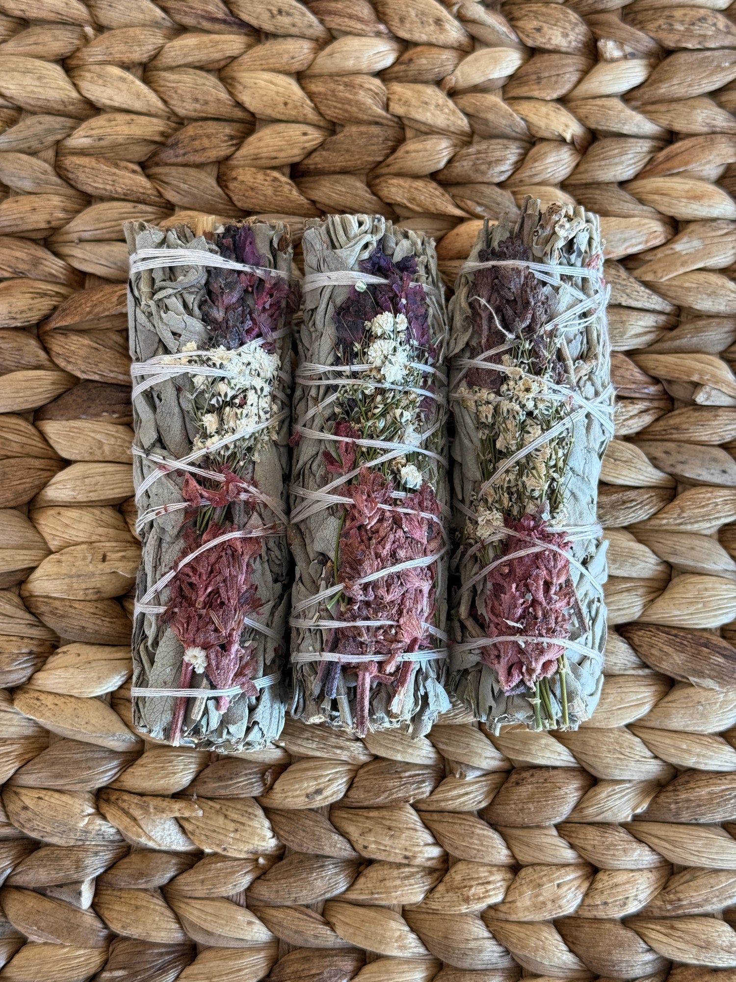 Trio of hand-tied consecrated white sage smudge sticks with floral accents, sustainably harvested and perfect for energy cleansing.