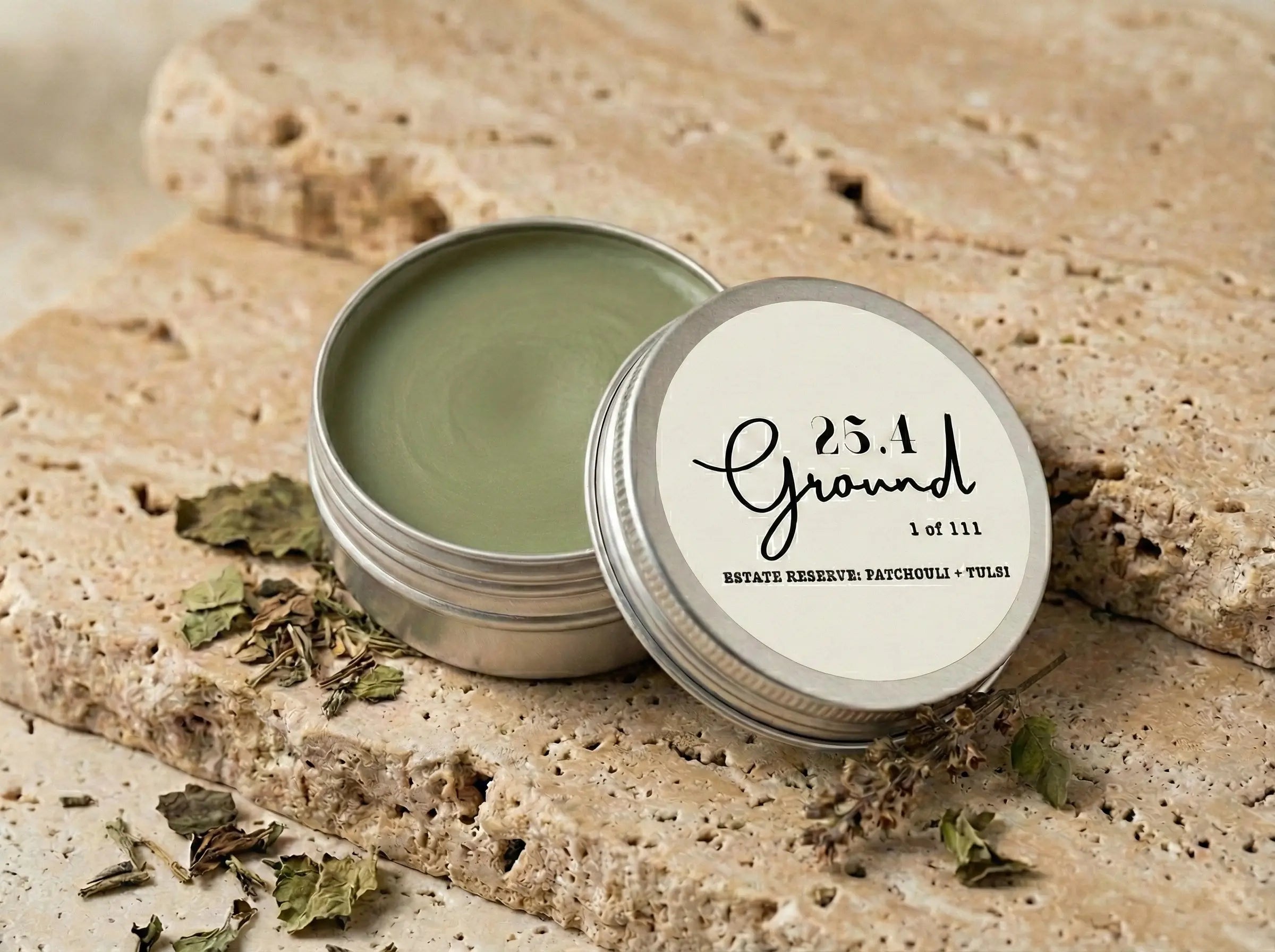 Macro shot of an open tin of 25.4 Ground Balm, revealing a deep, forest-green surface created by a 3-month cold infusion of whole Patchouli and Tulsi leaves.