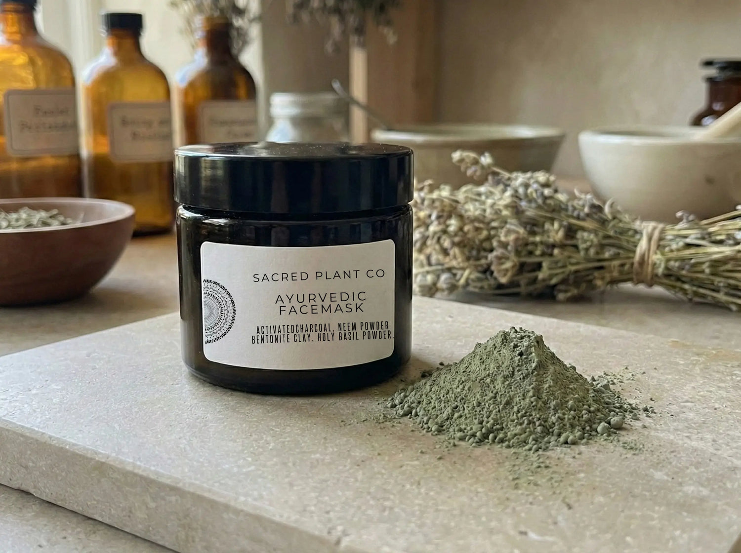 Front view of the black glass face mask jar sitting on a natural limestone slab with a sample of loose green herbal powder.