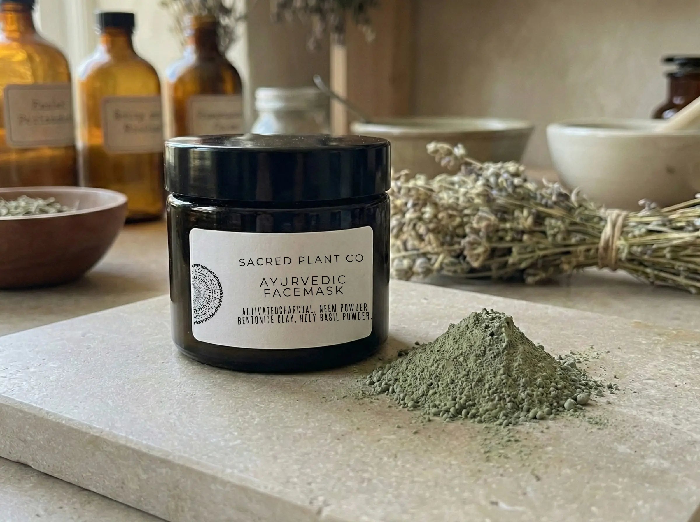 Front view of the black glass face mask jar sitting on a natural limestone slab with a sample of loose green herbal powder.