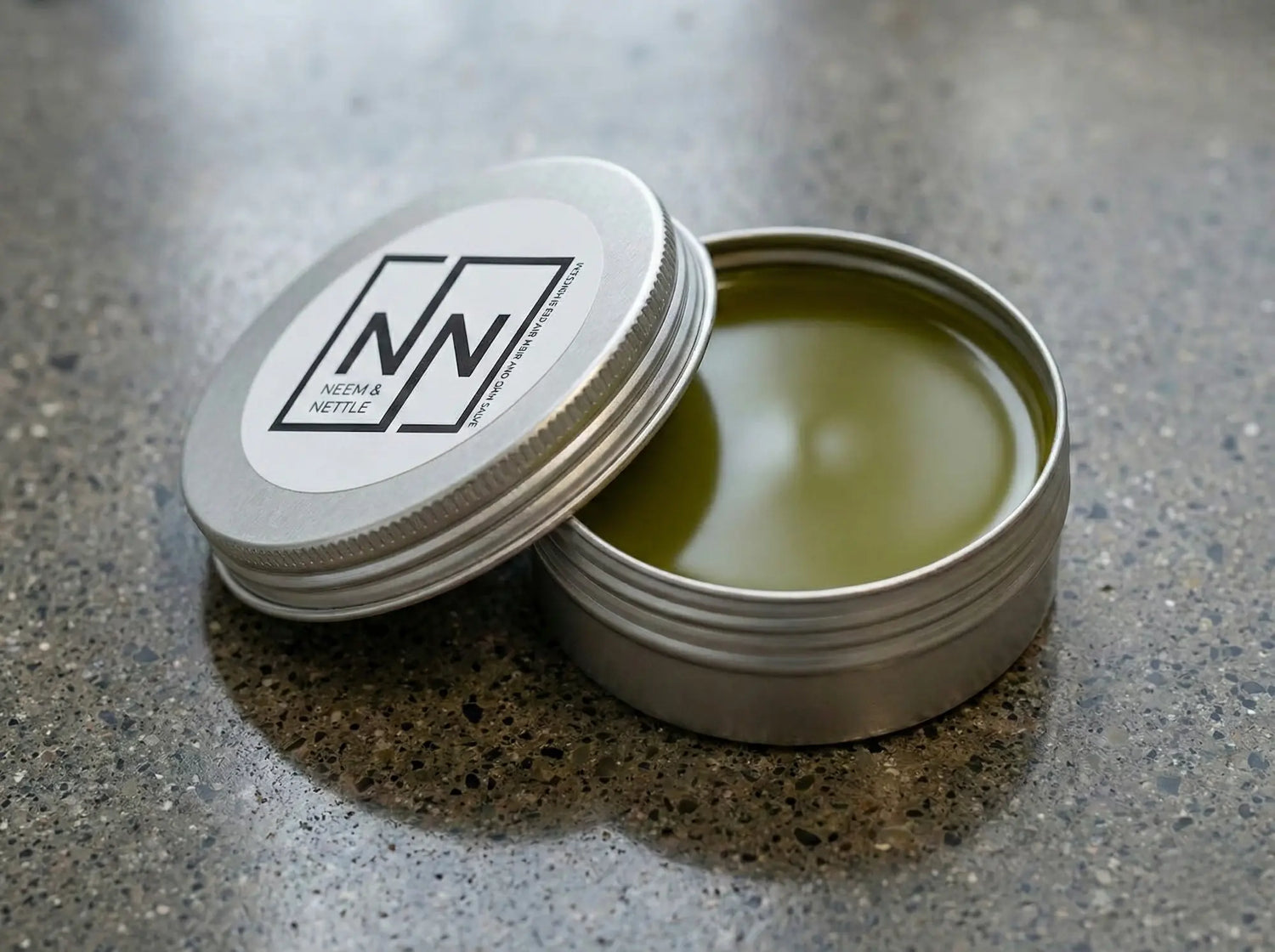 Close-up side view of an open salve tin showing the smooth, glossy surface of the nutrient-dense green herbal balm.
