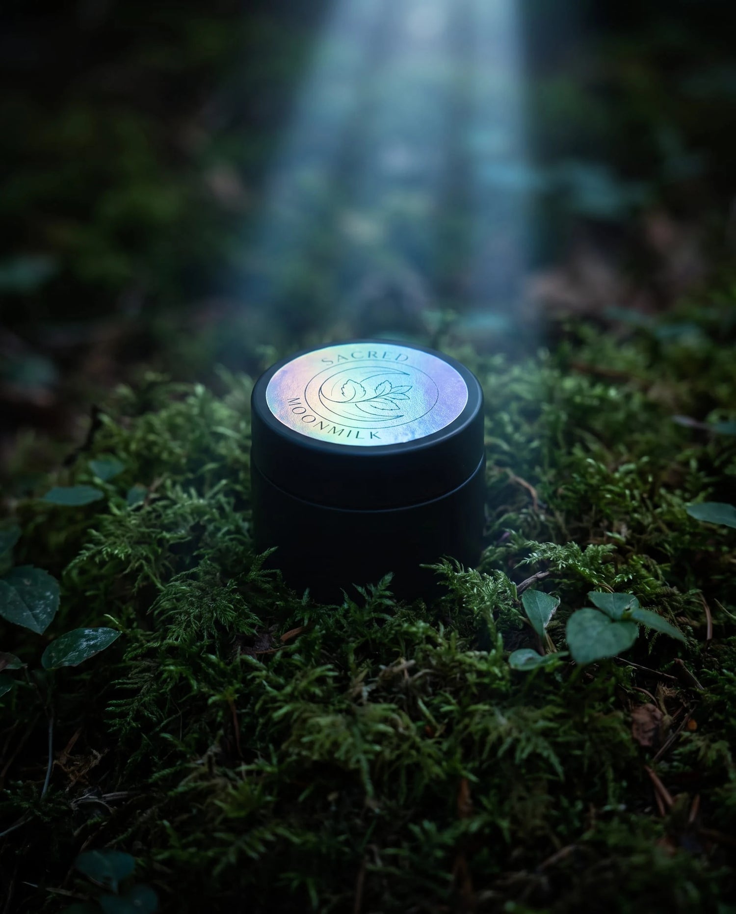 Closed Moonmilk Botanical Night Balm jar with holographic Sacred Moonmilk lid resting on green moss and ivy on the forest floor