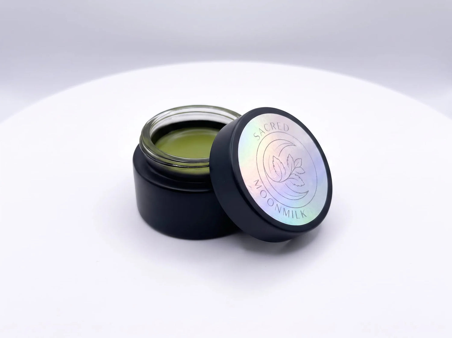 Open jar of Moonmilk Botanical Night Balm with holographic freshness seal, showing the small-batch golden balm