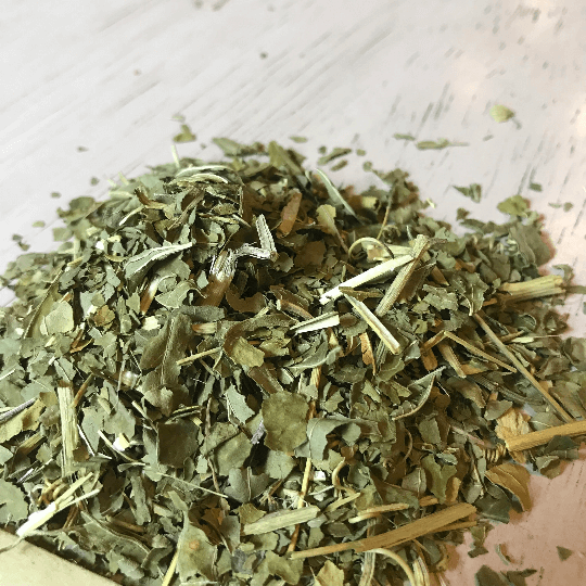 Loose Passion Flower leaves scattered on a white wood table, highlighting their fresh, green hues and natural texture at Sacred Plant Co.