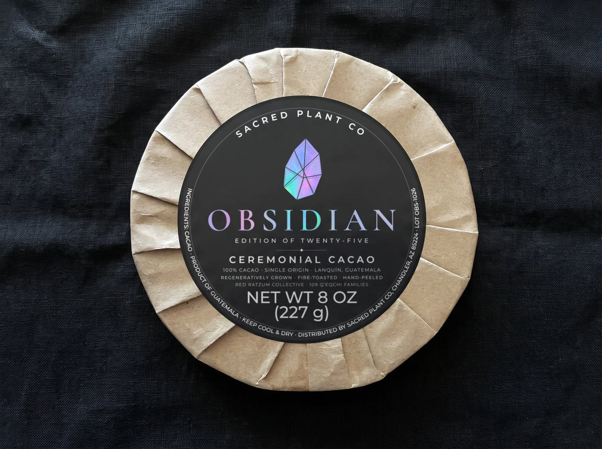 Obsidian Edition of twenty-five ceremonial cacao round on black linen, the holographic obsidian shard and foil lettering catching the light