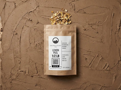Sacred Plant Co 1/2 lb bag of dried lemon peel lying flat on a textured clay surface. Small pieces of dried golden lemon peel spill naturally from the top of the kraft paper packaging, which features a label reading &
