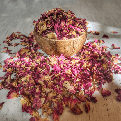 Dried pink rose petals in a wooden bowl, the Rosa damascena flowers steam-distilled into Sacred Plant Co rose hydrosol.