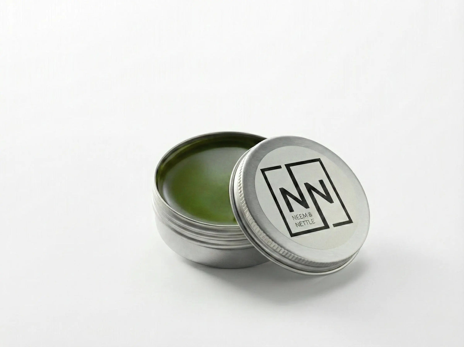 Open tin of Sacred Plant Co Neem &amp; Nettle Salve with the lid leaning against it on a neutral background.