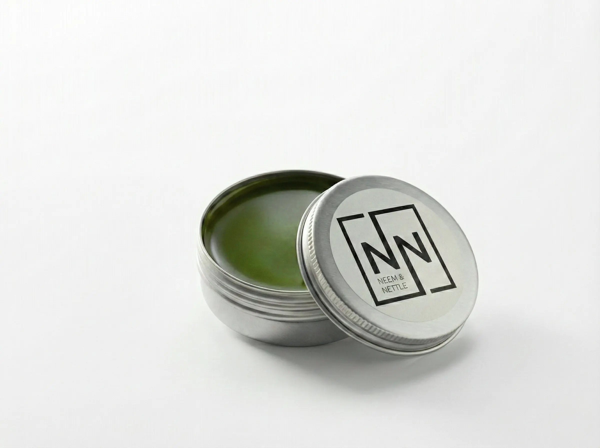 Open tin of Sacred Plant Co Neem &amp; Nettle Salve with the lid leaning against it on a neutral background.