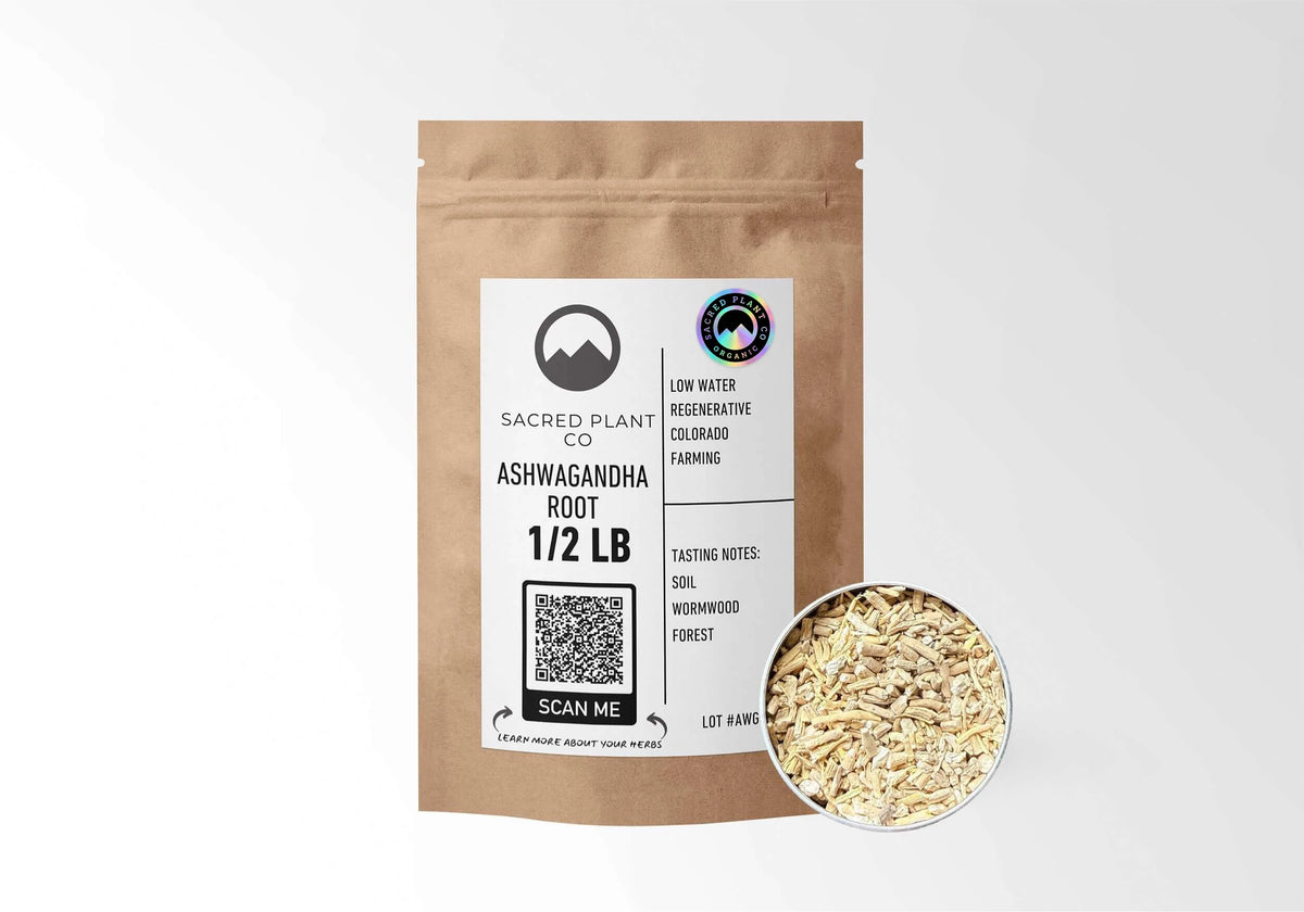 A 1/2 lb kraft pouch of Sacred Plant Co organic, cut Ashwagandha Root (Withania somnifera) displayed next to a sample of the chopped, dried pale root. The packaging label emphasizes low-water regenerative farming and lists earthy tasting notes of soil, wormwood, and forest.