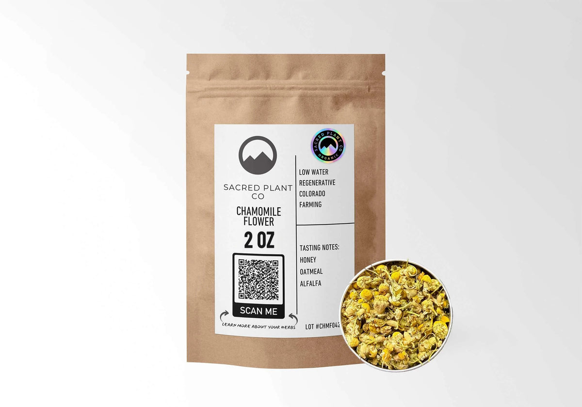 Sacred Plant Co Organic Chamomile Flower 2 oz in a kraft stand-up pouch with the holographic organic seal on the label and a sample of whole dried chamomile flowers in a silver tin.