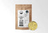 A 1/2 lb kraft pouch of Sacred Plant Co organic, cut and sifted Licorice Root (Glycyrrhiza glabra) shown next to a sample of the dried yellow root. The label highlights low-water regenerative farming and lists tasting notes of stevia, vanilla, and earth.