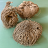 Three dried Resurrection Plants (Selaginella lepidophylla) displayed on a soft green surface, highlighting their intricate, coiled fronds and natural earthy texture.