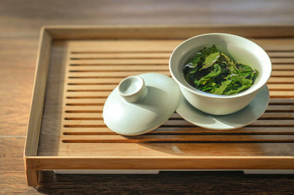 A serene setting featuring a white porcelain cup filled with steeped loose leaf Sencha green tea, placed on a bamboo tea tray, illustrating the elegance of Japanese tea tradition.