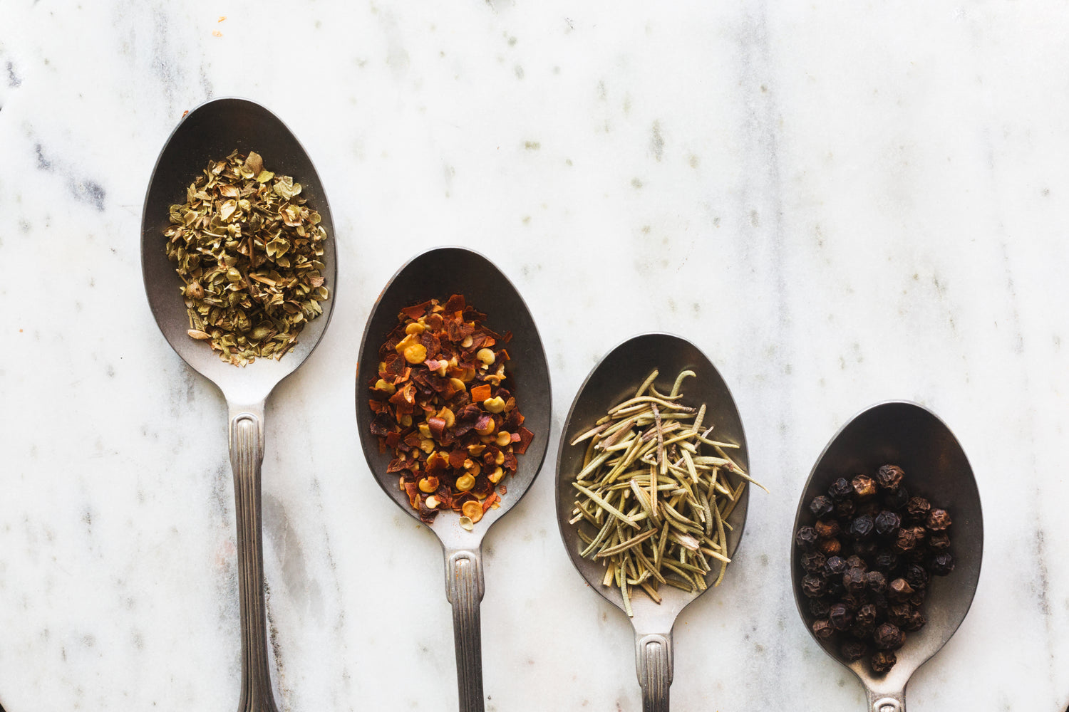 Dried herbs delicately arranged on shiny metal spoons, showcasing the exquisite variety and quality of our wholesale offerings.