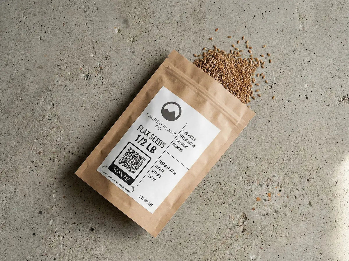 Angled view of Sacred Plant Co flax seed pouch on a textured surface, highlighting labels for regenerative farming and low water usage.