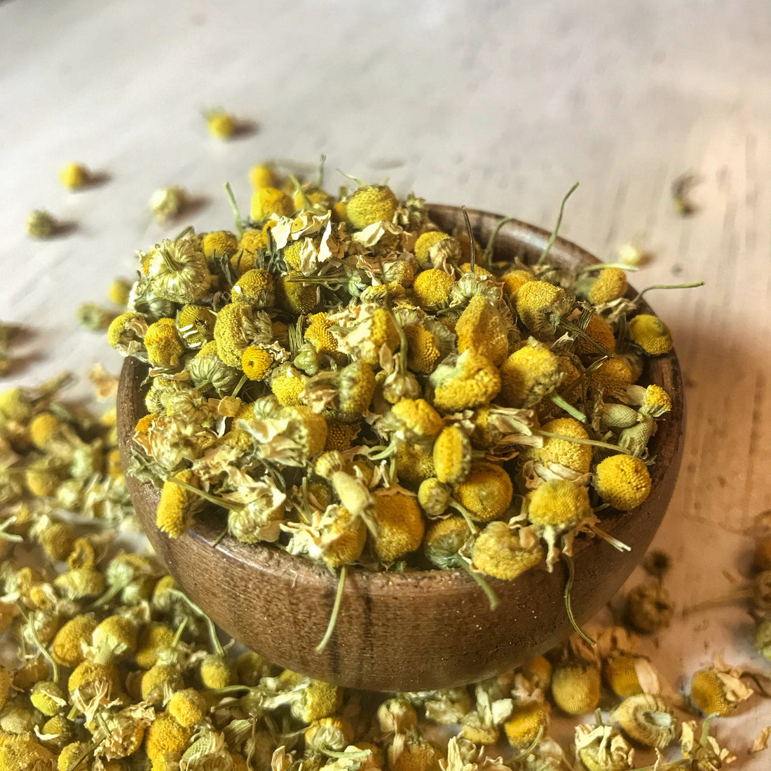 Close-up of a wooden bowl overflowing with aromatic dried chamomile flowers, perfect for a relaxing tea or natural skincare.