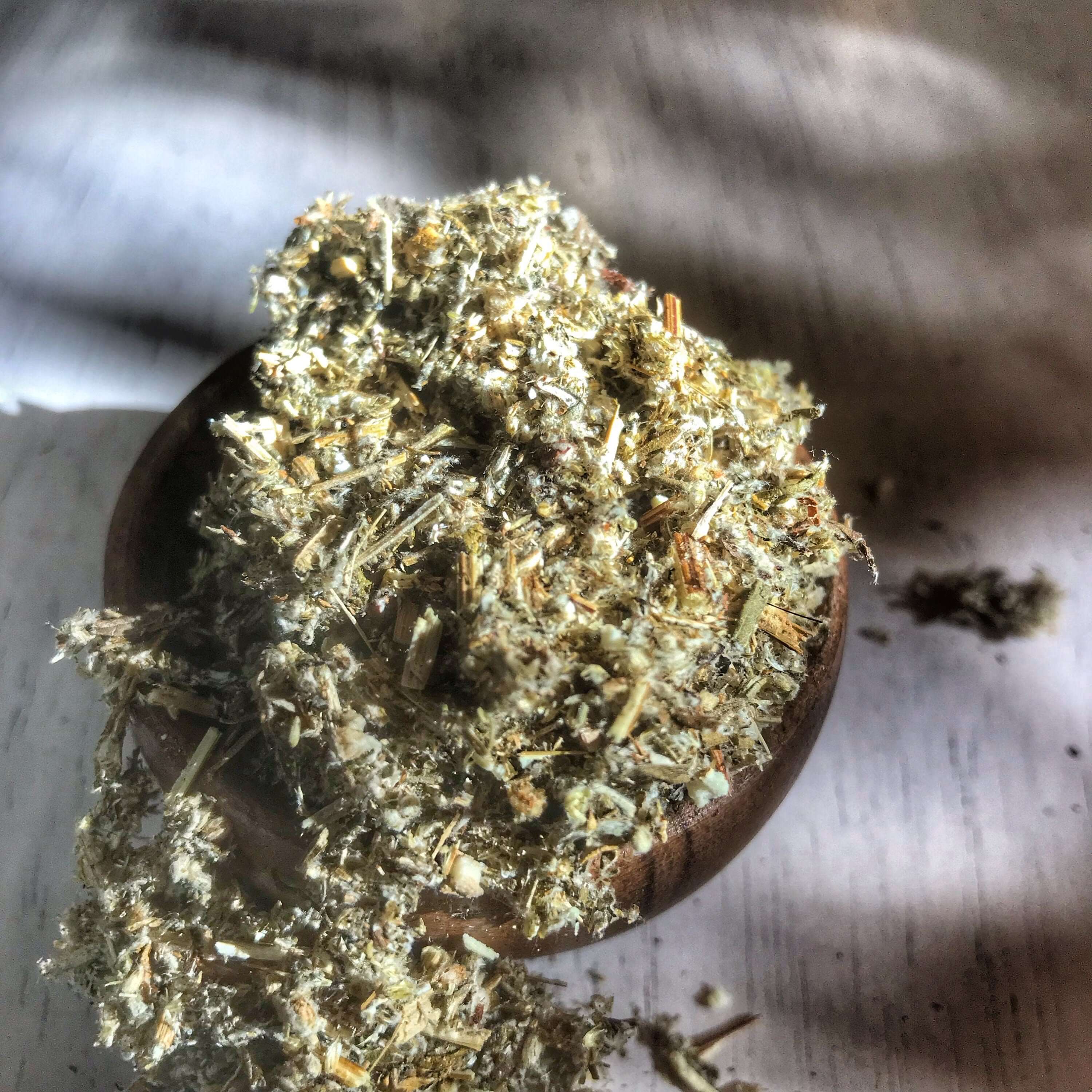 Mugwort Herb spilling from a rustic wooden bowl, highlighting the herb&