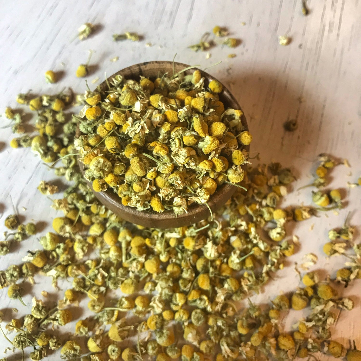 Top view of a bowl full of dried chamomile flowers, showcasing the natural yellow hues and quality of the organic blossoms.