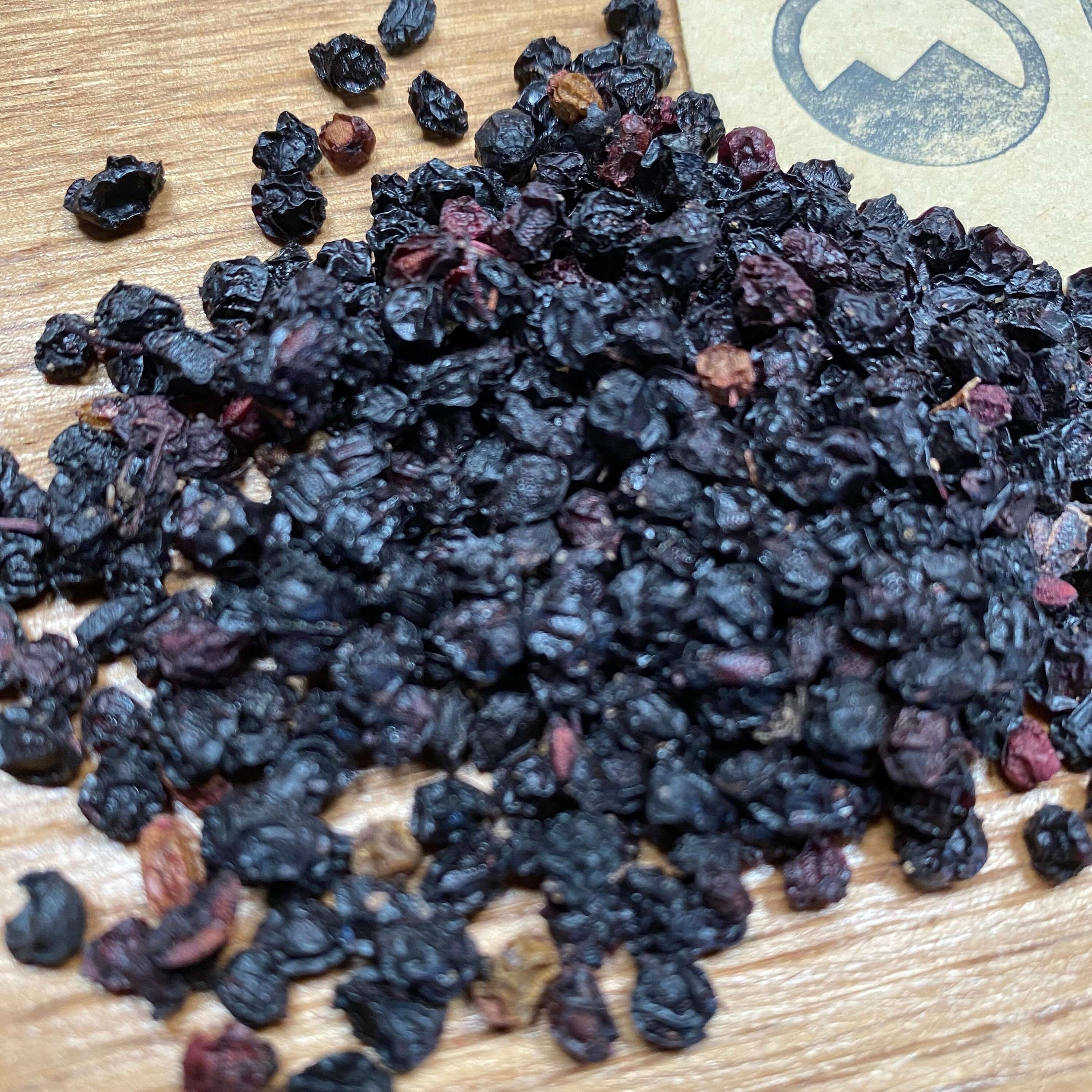Dried Whole Elderberries placed on a wooden background, rich dark texture complementing Sacred Plant Co’s premium herb quality.
