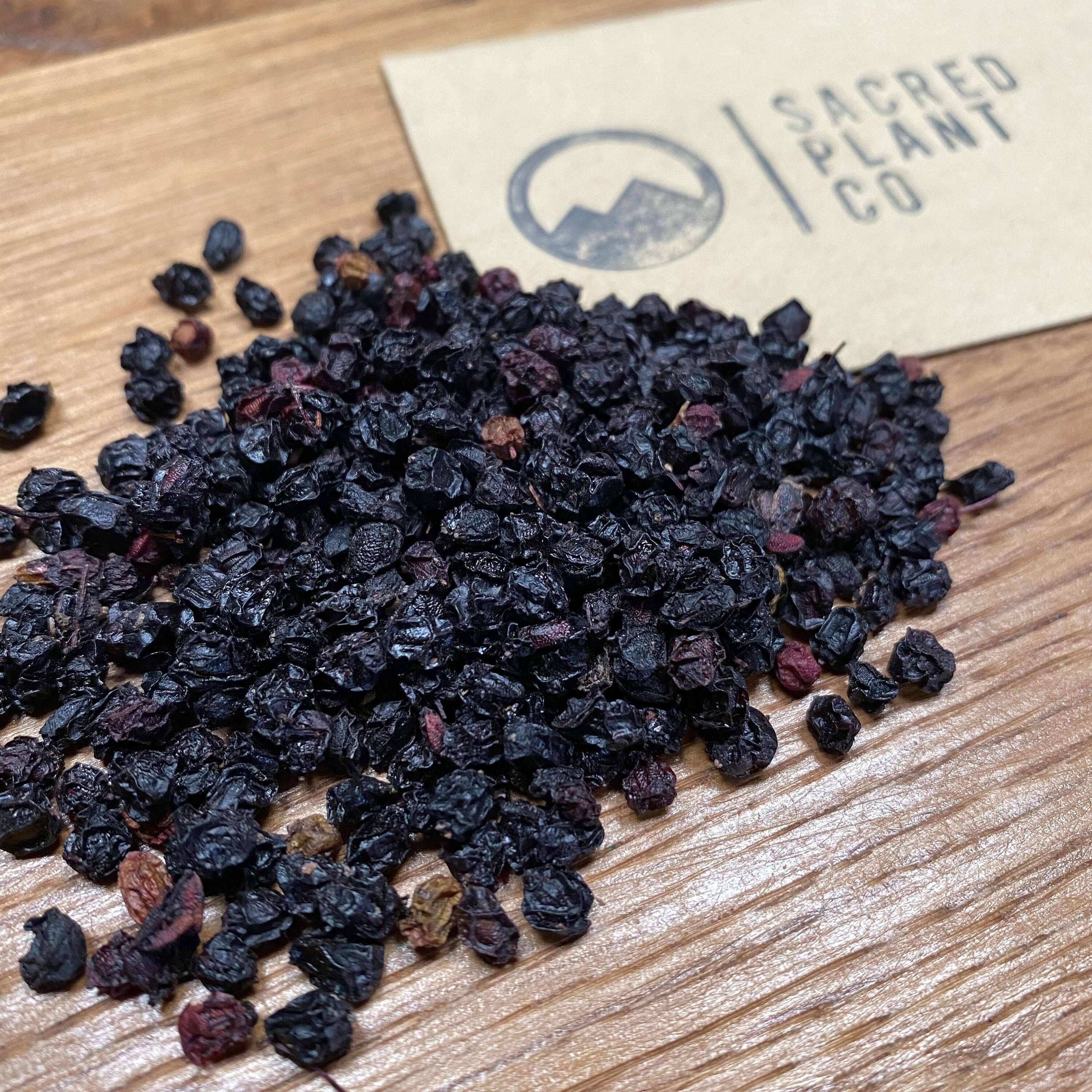 Premium dried Whole Elderberries scattered on wood, highlighting Sacred Plant Co’s commitment to high-quality natural products.