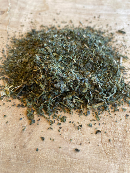 Close-up of dried and cut stinging nettle leaves scattered on a wooden surface, showcasing the texture and natural green color of the herbal remedy.